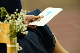 Eine Konfirmandin hält die Urkunde und das Kreuz in der Hand