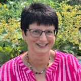 Frau mit kurzen schwarzen Haaren und rosa Blusa